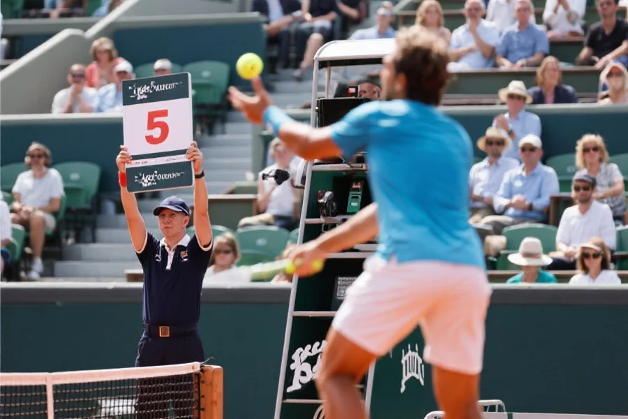 网球比赛现场裁判举牌记分，前景为网球运动员准备发球，背景为观众席